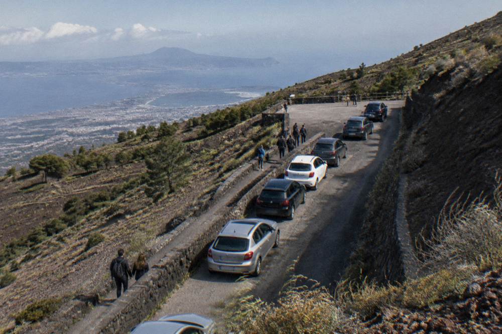 Rowed cars parked along a narrow mountain road with volcanic slopes rising behind
