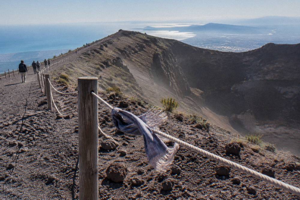 Hikers on the Gran Cono trail walking up the dark gravel slope toward the Vesuvius crater rim