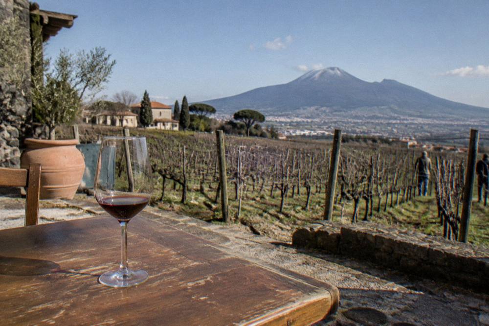 A wine glass on a rustic table with the ridge of Mount Vesuvius in the background
