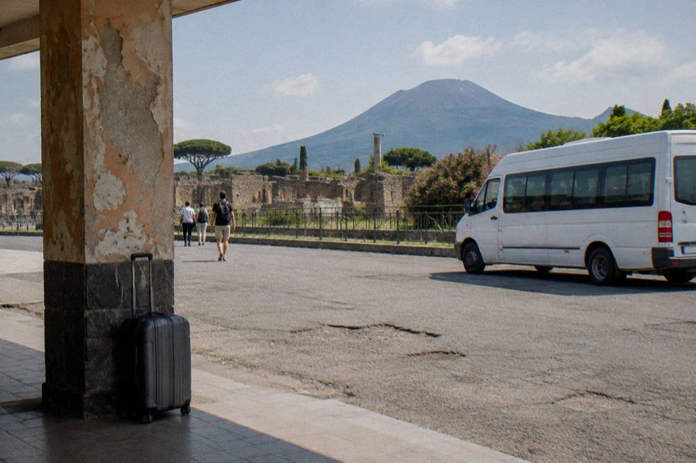 A minibus on a road above Pompeii with the excavations and Vesuvius behind