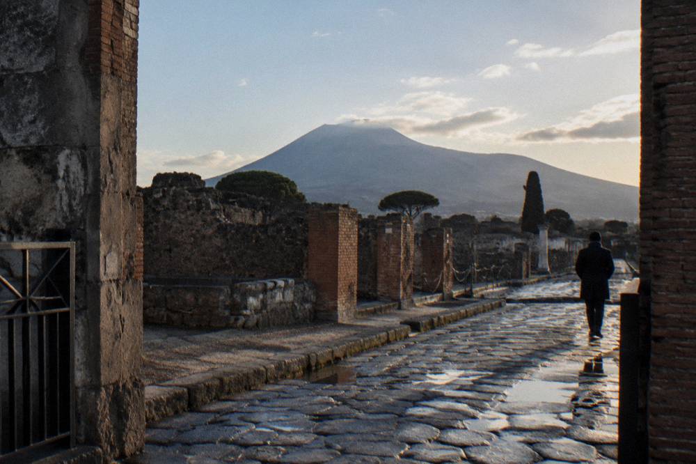 Ruined stone walls of an ancient Roman town with Mount Vesuvius rising in the background.
