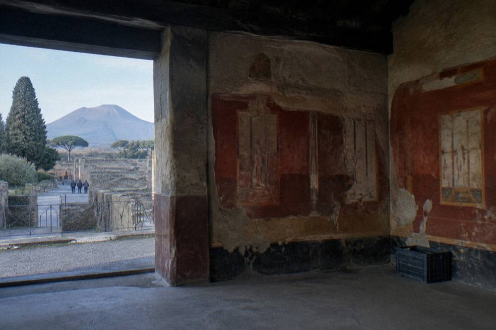 Frescoed wall fragments inside a roofed ancient Roman ruin.