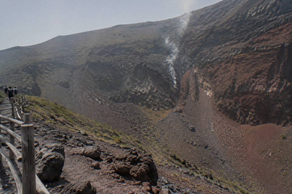 Steep ash and lava slopes rising toward a wide crater rim under hazy sky