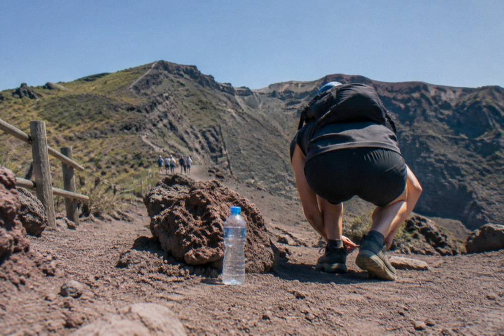 Hikers in sturdy shoes on a dusty volcanic path beside a rocky slope