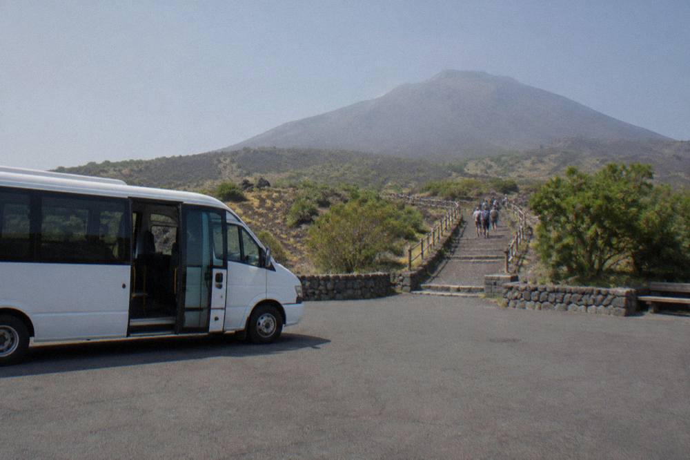 A shuttle bus parked at the Quota 1000 plaza on the slopes of Mount Vesuvius with the trailhead ahead