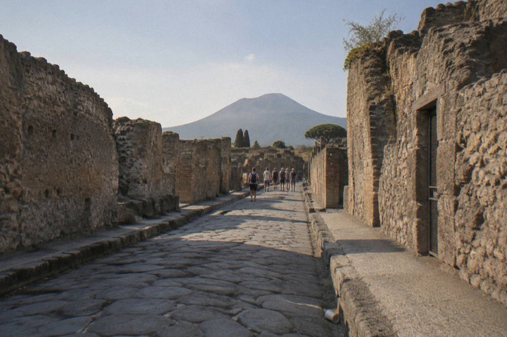 A guided group walking the stone streets of the Pompeii excavations with Mount Vesuvius rising behind the ruins