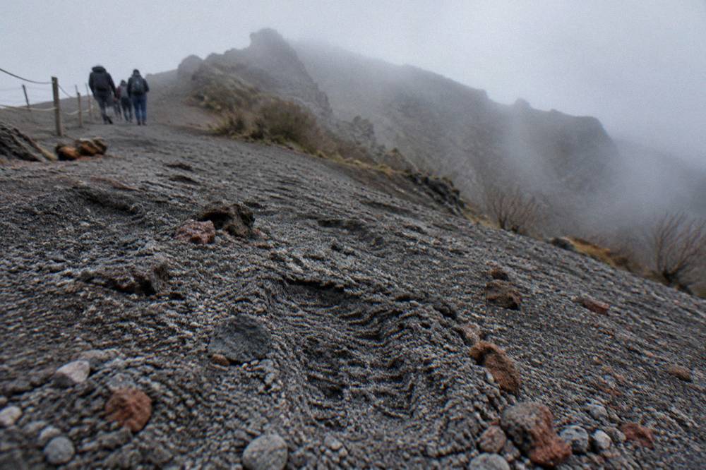 Loose grey volcanic gravel covering the crater trail with boot prints worn into the surface