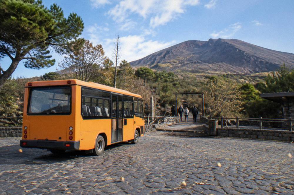 A small shuttle bus parked at a mountain plaza on Vesuvius with the trailhead beyond