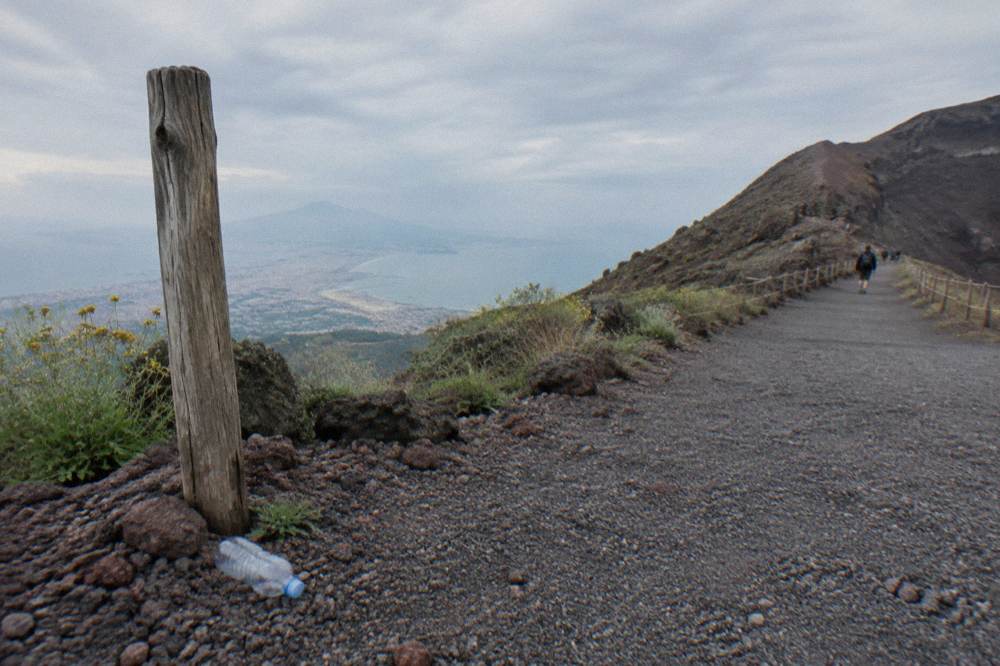 A wide gravel trail curving up the flank of Vesuvius with the Bay of Naples hazy in the distance
