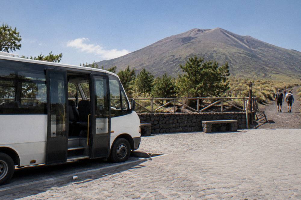 A shuttle bus parked at a stone plaza on the Vesuvius access road below the crater trailhead
