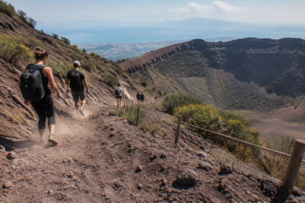 Hikers descending the ash path from the Vesuvius crater rim in late afternoon light