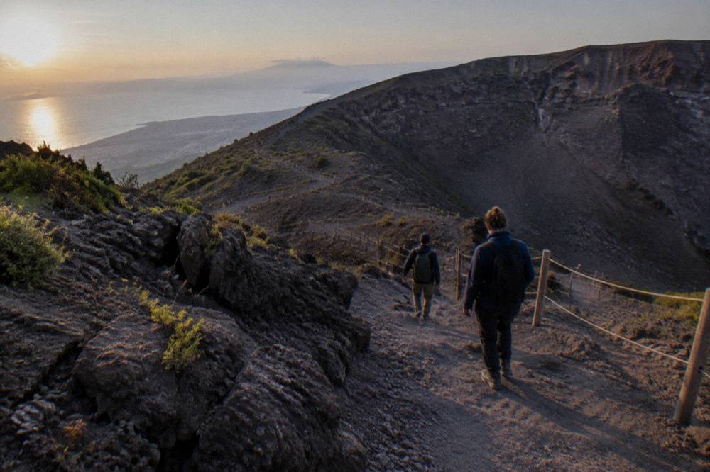 Hikers in jackets descending the crater path as shadows lengthen on the ash slope