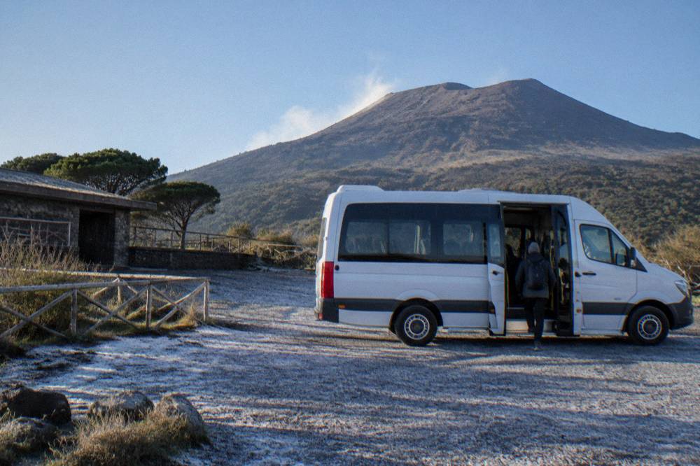A shuttle bus parked at the Quota 1000 plaza with the volcano slope rising behind it
