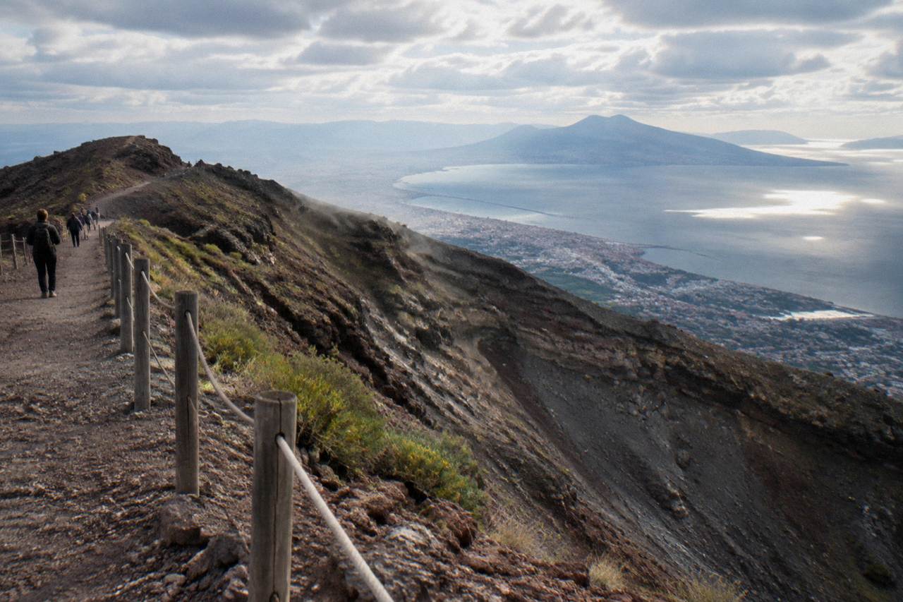 The Gran Cono crater path on Mount Vesuvius under a partly cloudy sky above the Bay of Naples