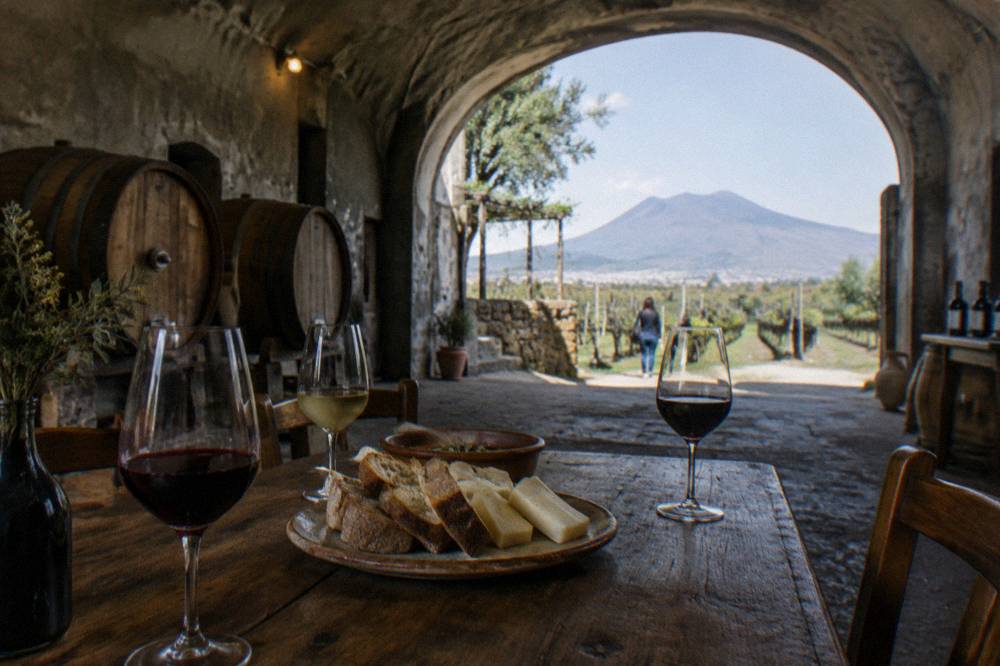A tasting table set with glasses of red and white wine beside a platter of local bread and cheese