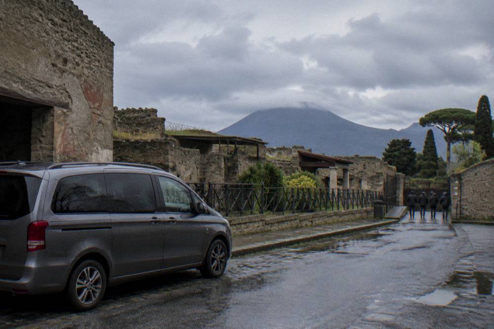 Small minivan parked on a road beside ancient stone walls