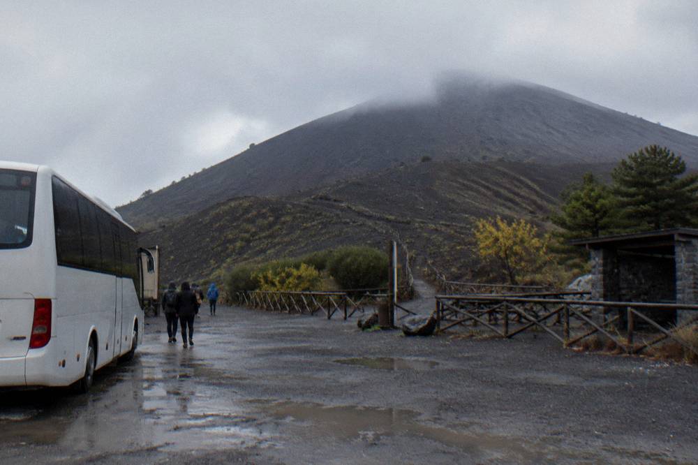 A coach parked at the Quota 1000 plaza with the volcano slope rising behind
