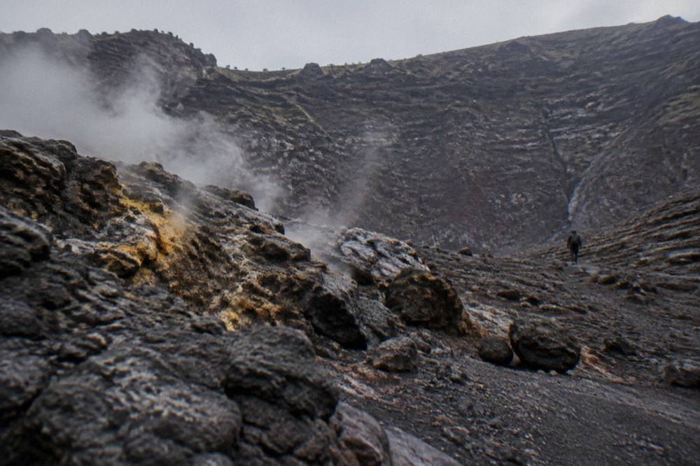 The crater rim of Vesuvius with dark volcanic rock and steam rising from the inner slopes.