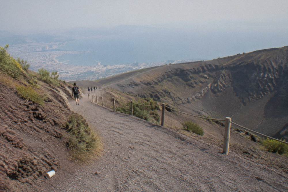 A wide gravel path climbing the slope of Vesuvius with the Bay of Naples visible below.