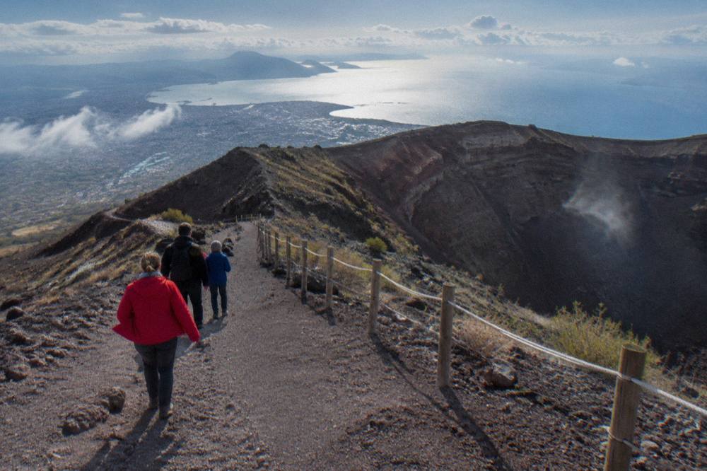 A family walking the crater path of Vesuvius with the Bay of Naples below