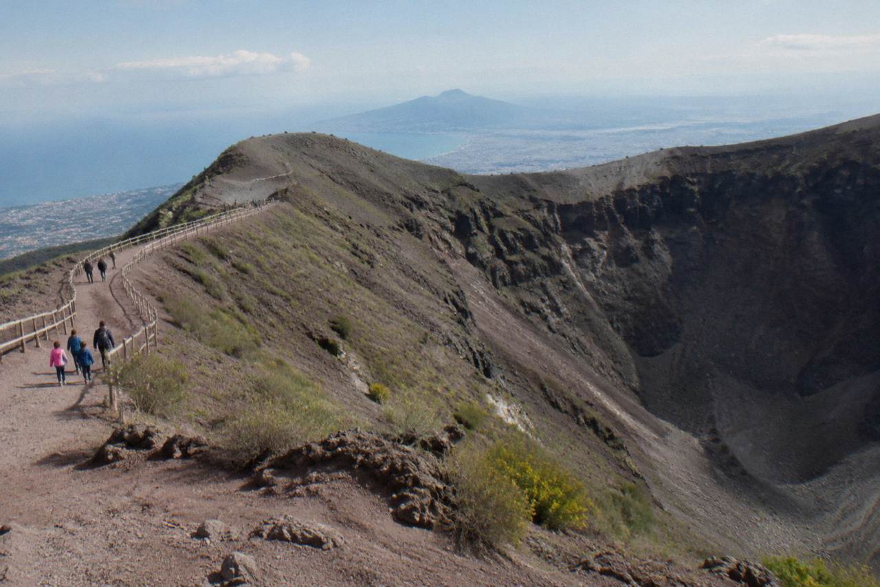 A wide volcanic crater rim path under a clear sky with ash slopes below