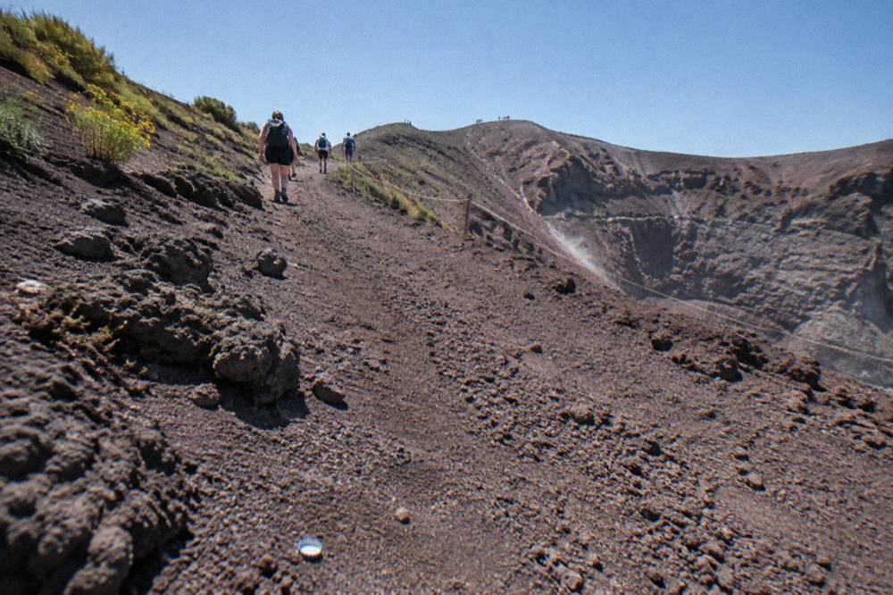 Walking group on the ash path toward the Vesuvius crater rim under a clear sky