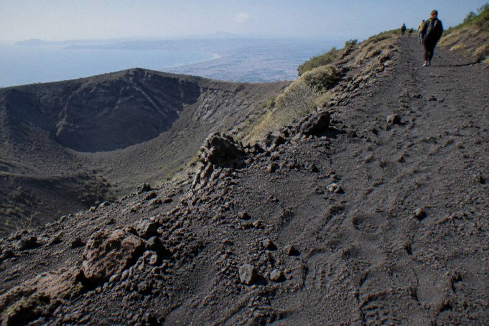 Volcanic ash trail surface rising toward the crater rim with the bay below