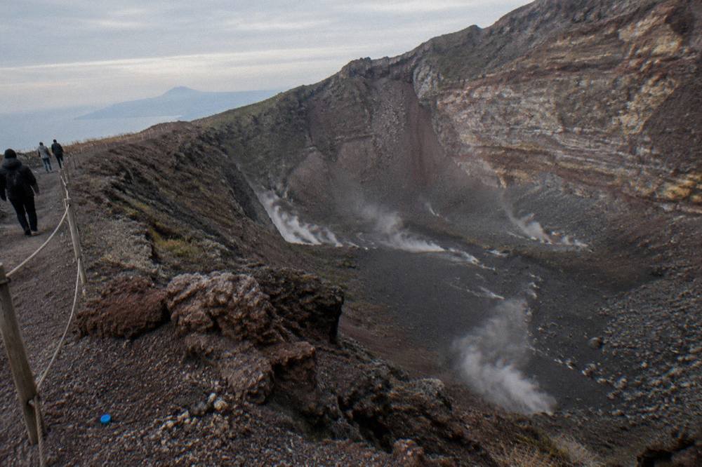 The steaming crater of Vesuvius seen from the Gran Cono trail with dark volcanic ash slopes