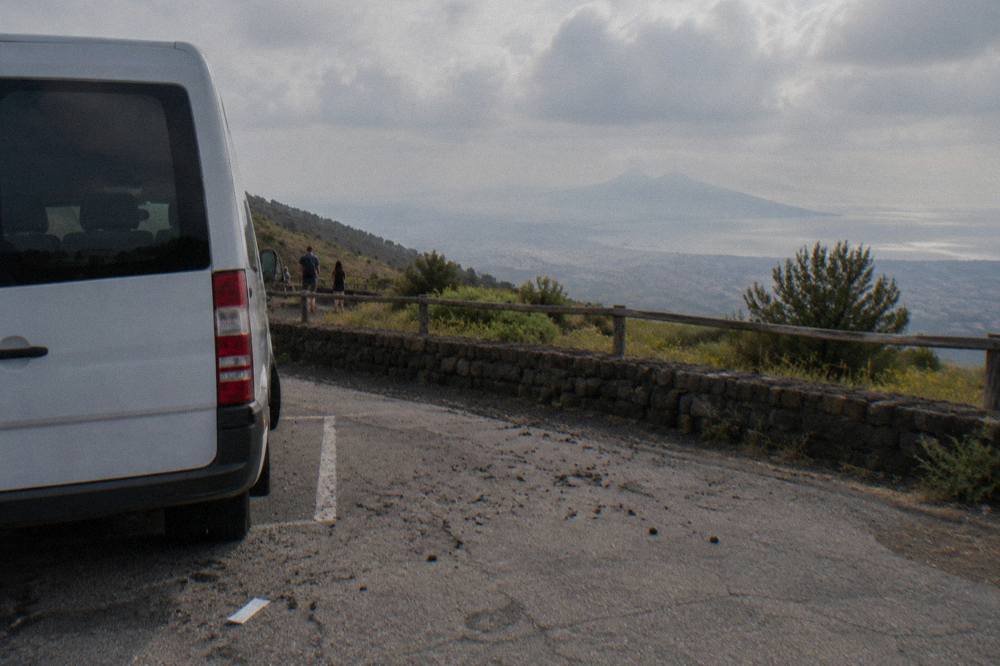 A tour minibus parked on the volcanic slope of Mount Vesuvius with the Bay of Naples below