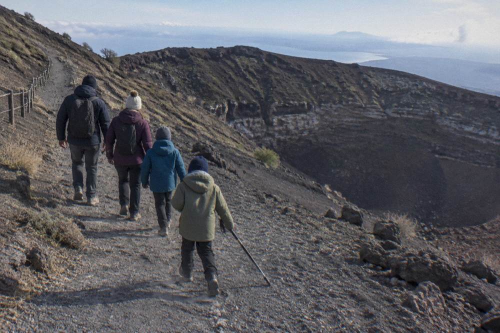 A family in jackets and hats walking together on the wide crater path below the Vesuvius rim