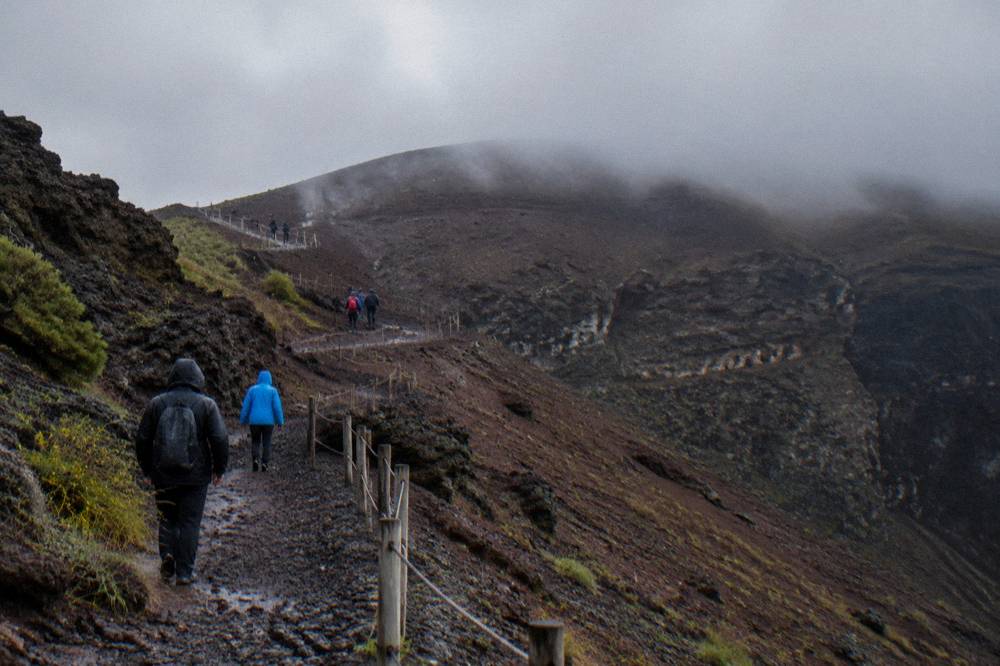 The Vesuvius crater trail under low autumn cloud with walkers in rain jackets on the path