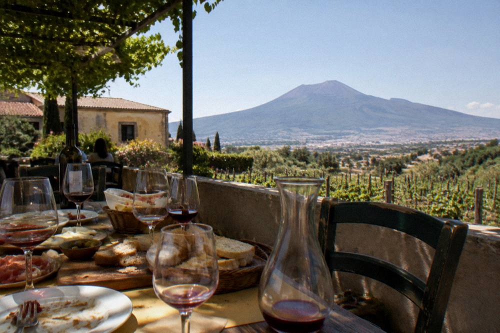A table set with wine glasses and a lunch spread on a terrace overlooking Vesuvius