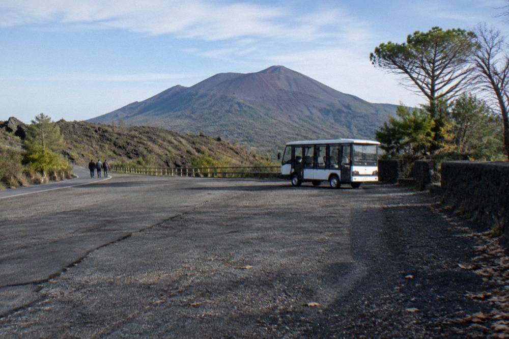 A gravel parking area on a volcanic slope with shuttle vehicles and the upper trail road beyond
