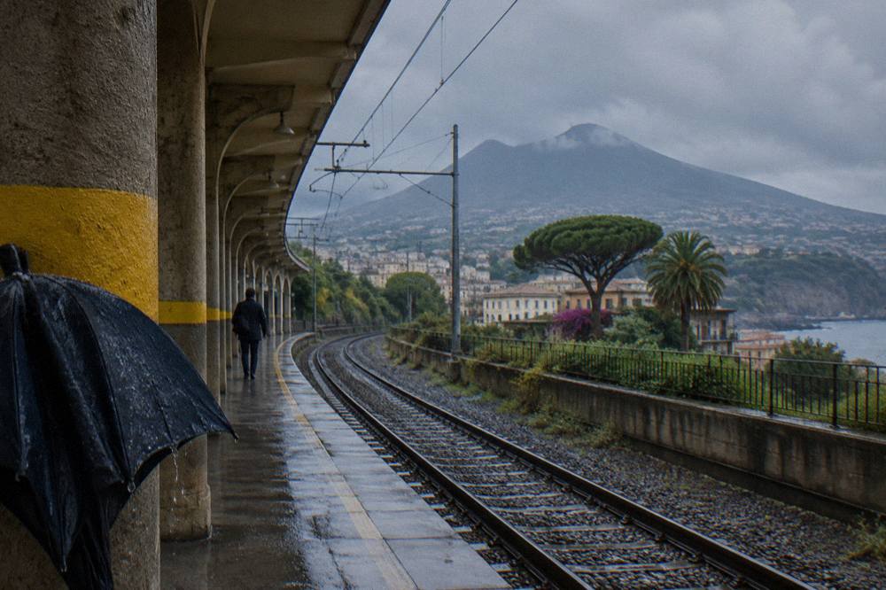 Train platform at a Circumvesuviana station with tracks leading toward hills