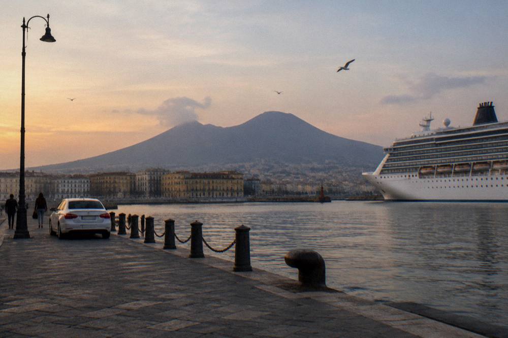 Cruise ship at a quayside with a city skyline and volcano shape behind it